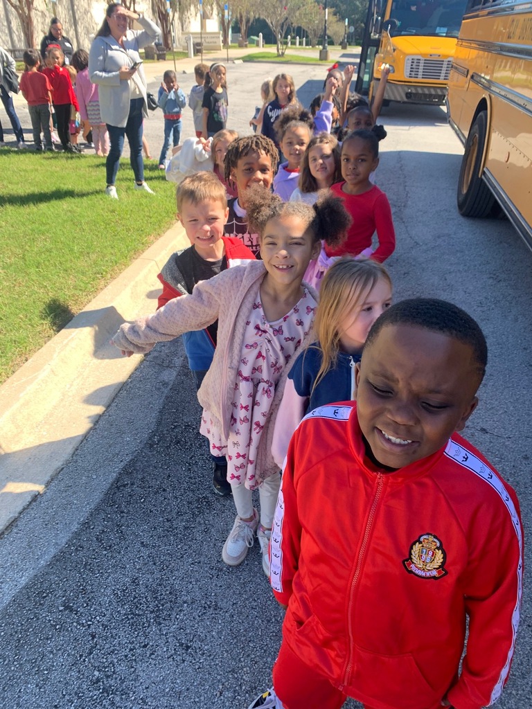 A group of children standing in a line next to a school bus on the street.