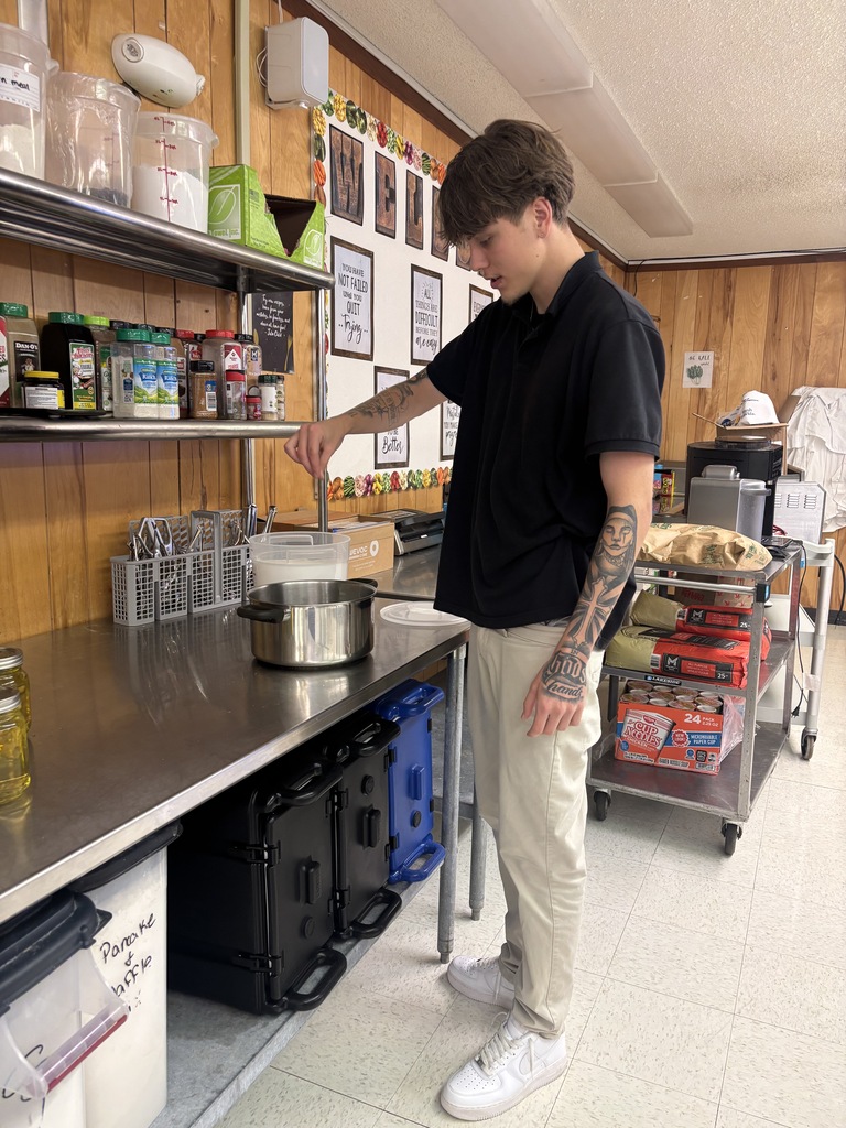 Person in a kitchen stirring a pot of food while standing at a counter.