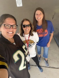 Three women standing close together, smiling for a photo, wearing sports jerseys and glasses.