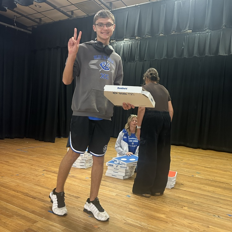 Person holding pizza box in front of a seated person. Two more people are standing behind them.