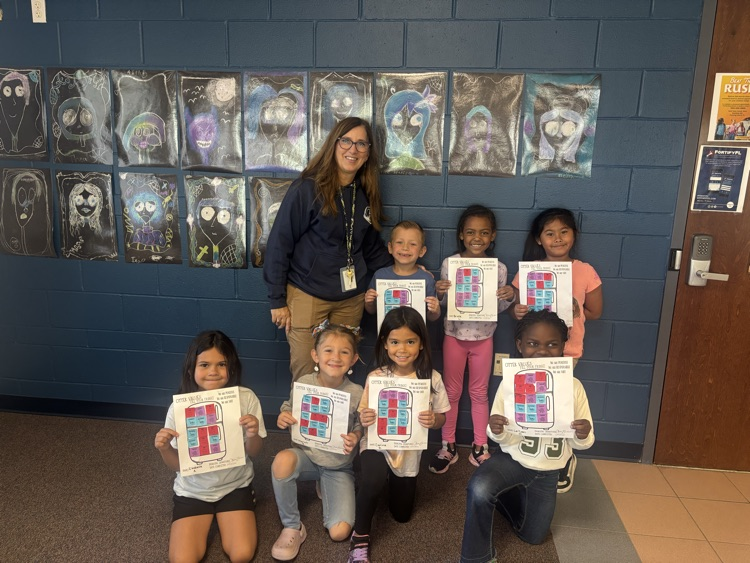 Students and a teacher hold framed artwork in a room with blue walls and framed art.