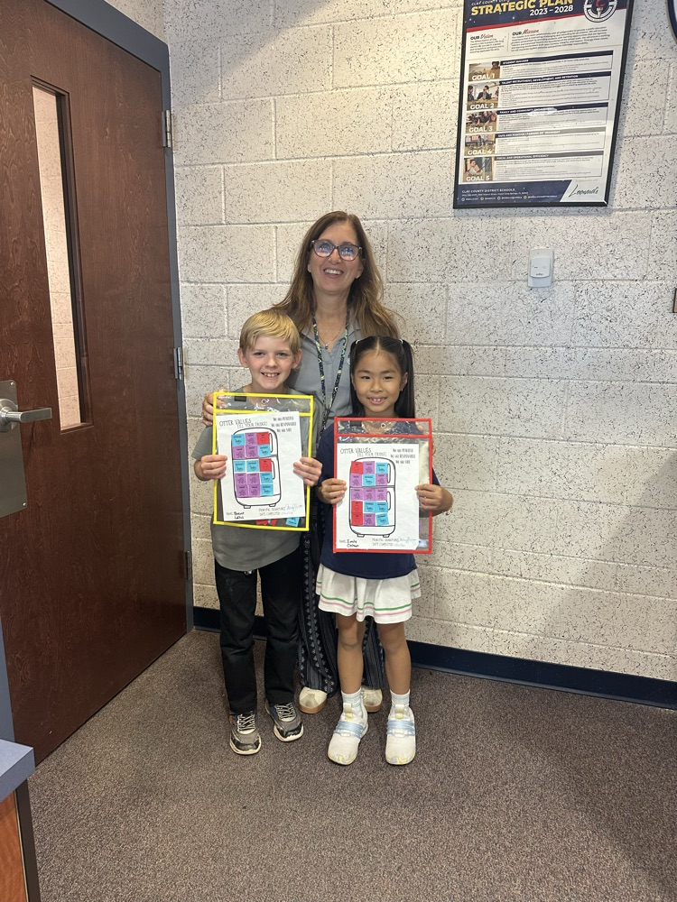 Woman with glasses stands with two children, one holding a yellow folder and the other a red folder.