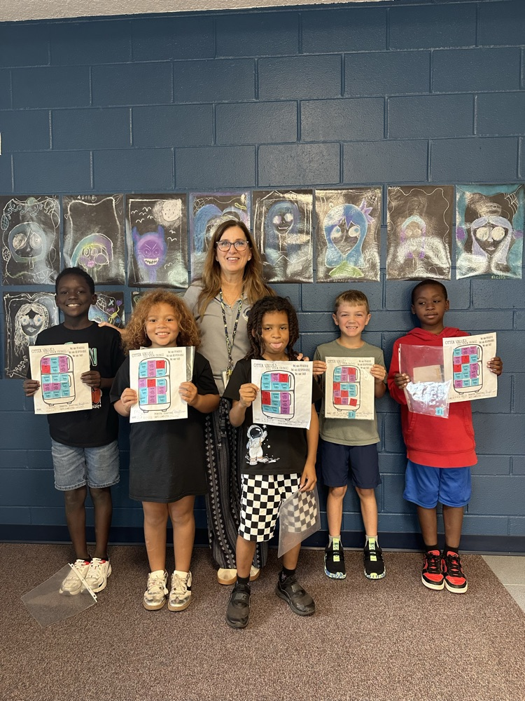 Six students in shorts and sneakers hold up art projects in front of a teacher.