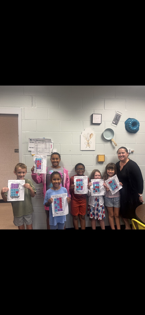 Students with their artwork pose for a group photo in a classroom with a white wall.