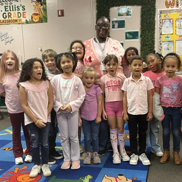A group of children stand in a classroom, posing for a picture with a smiling adult.