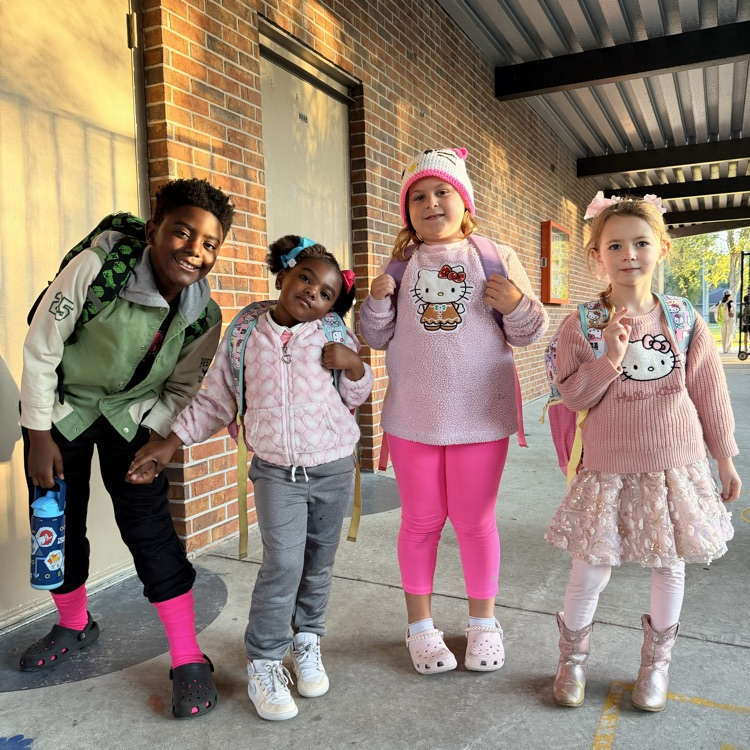 Five children stand outside a school building, two wearing pink pants, another with a Hello Kitty sweater.