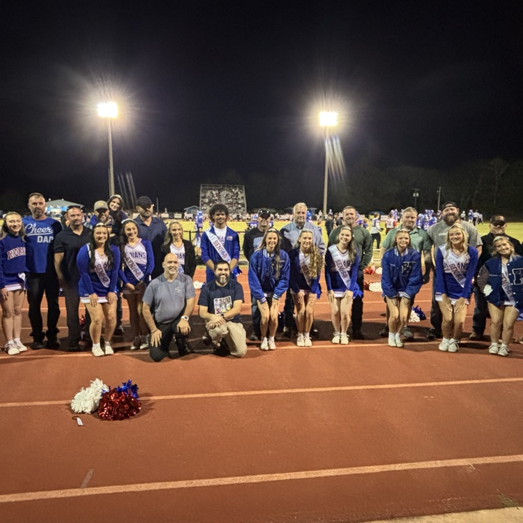 A group of people in blue uniforms, some wearing sashes, pose for a photo on a track.