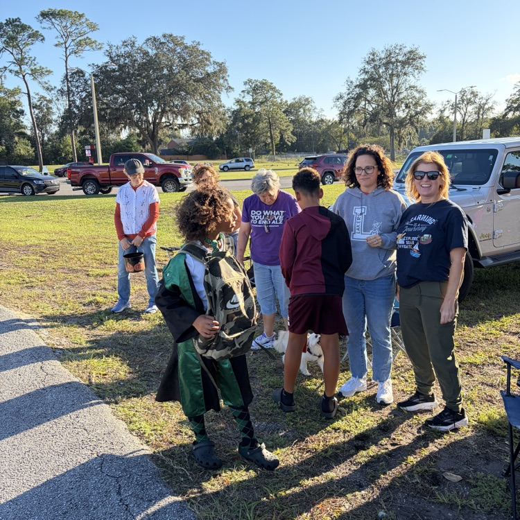 People stand outside near a pickup truck and a grassy area with trees, some wear glasses.