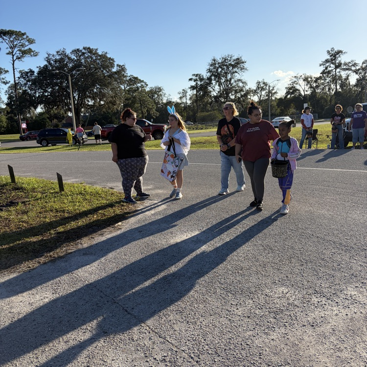 People walking on road near trees; one holding shopping bags, one holding child, one with dog.