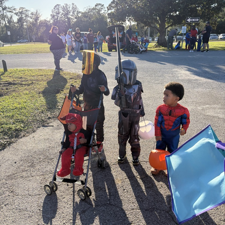 Children in costumes standing on a path. One holds a pumpkin and another holds a kite.