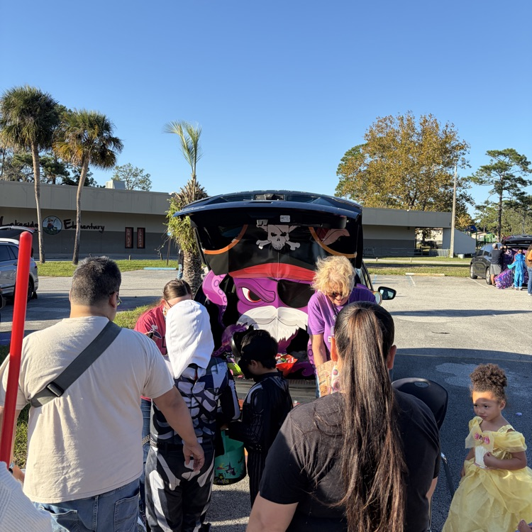 A group of children and adults, including some in Halloween costumes, in a parking lot.