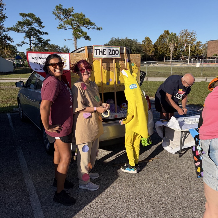 Four adults, two in animal costumes, stand by a vehicle with a cardboard box reading The Zoo.
