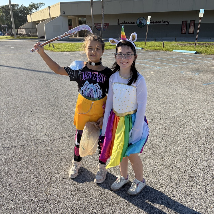 Two children in costumes standing in a parking lot in front of a building.