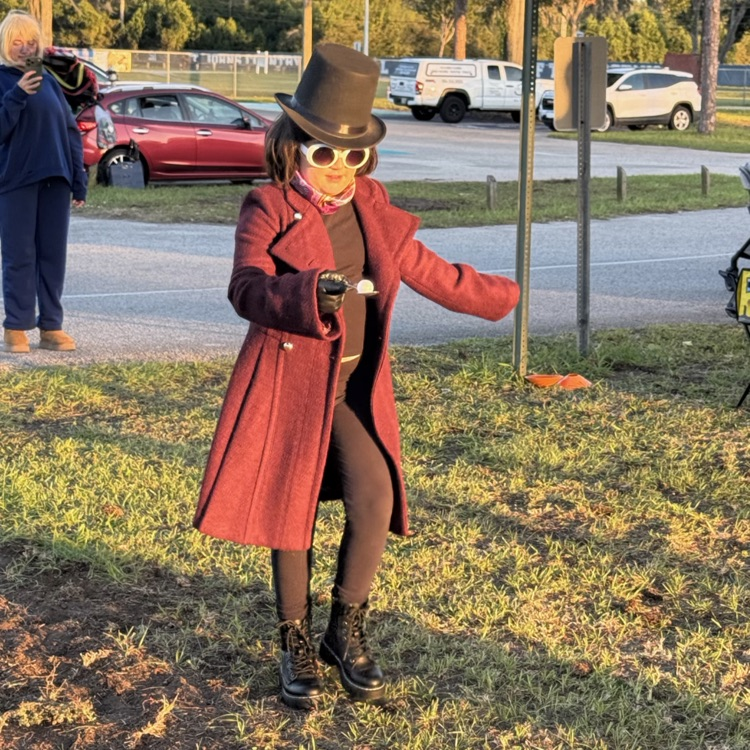 Person in red coat and top hat poses for a picture while another person holds a backpack.
