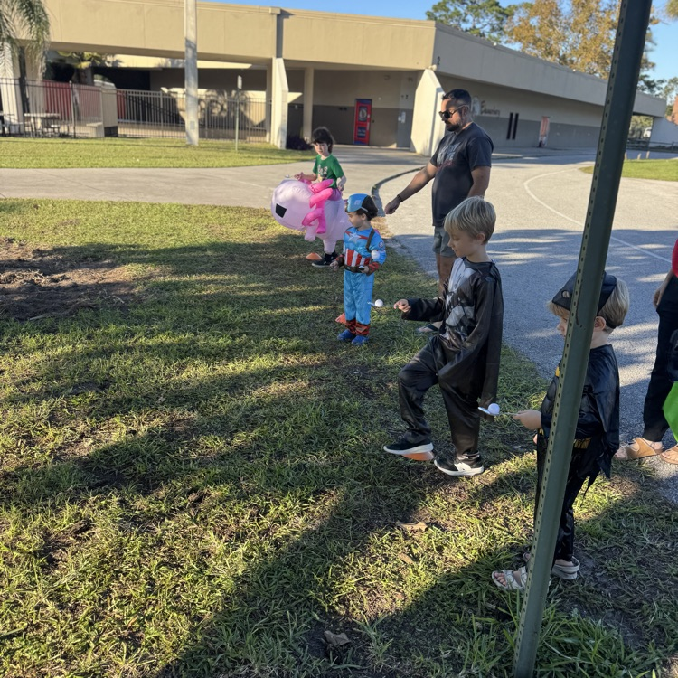 A group of children and a man wearing superhero costumes stand on a grassy field.