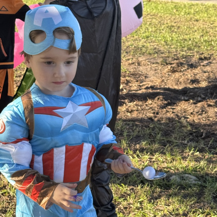 A child in a blue costume with a white star on the chest holds a silver spoon.