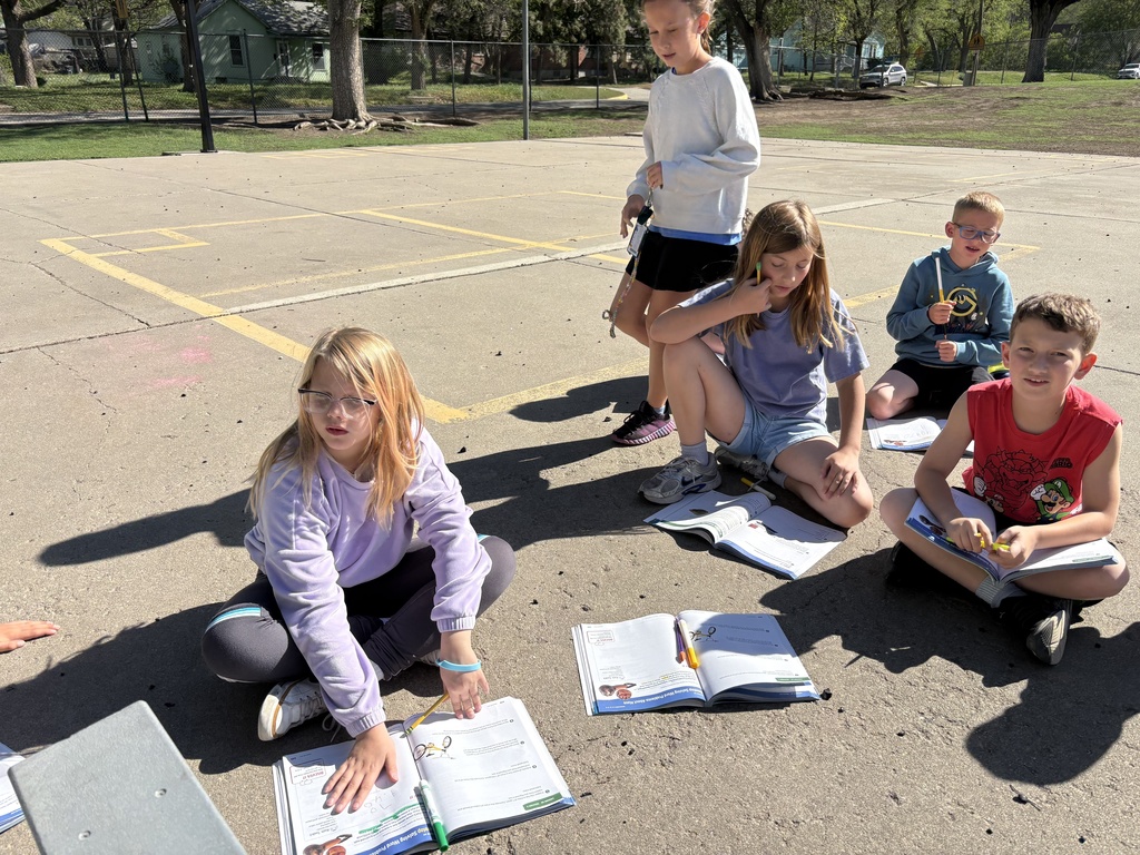 Students are sitting on the concrete area enjoying the nice weather while working on a math assignment together.