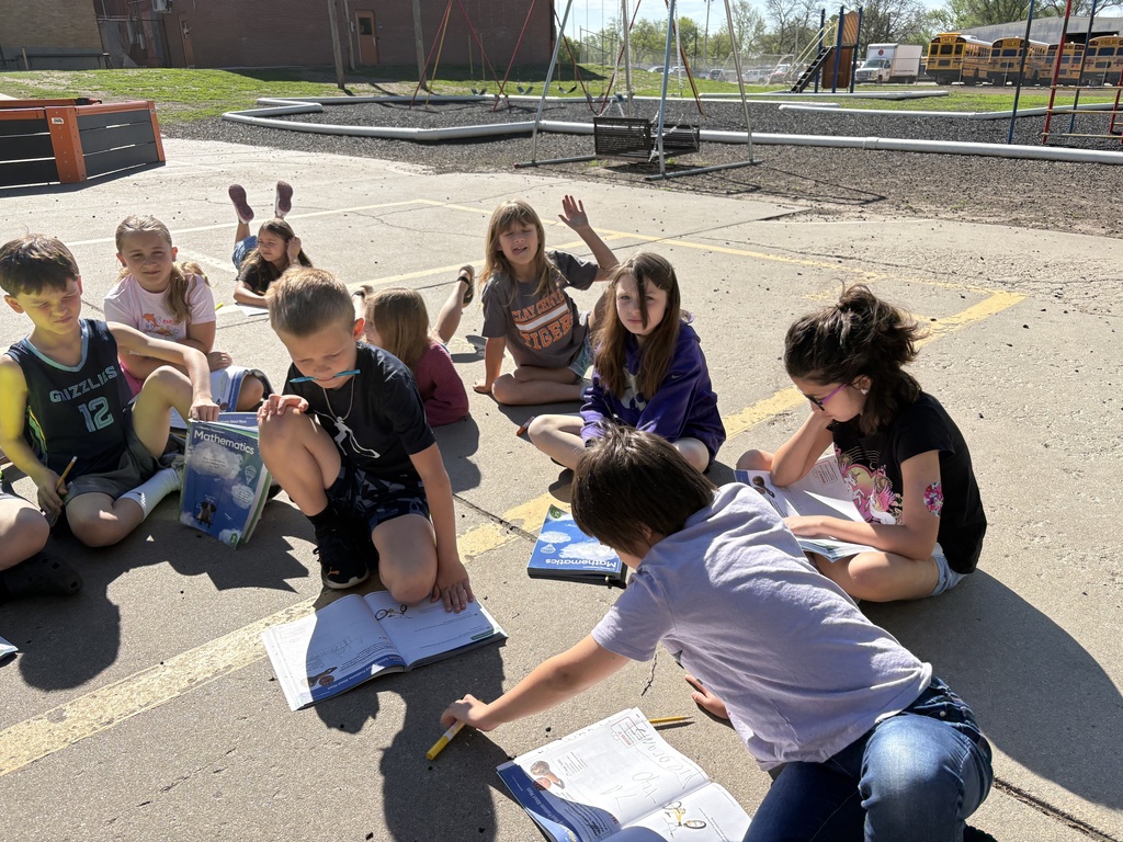 Students are sitting on the concrete area enjoying the nice weather while working on a math assignment together.