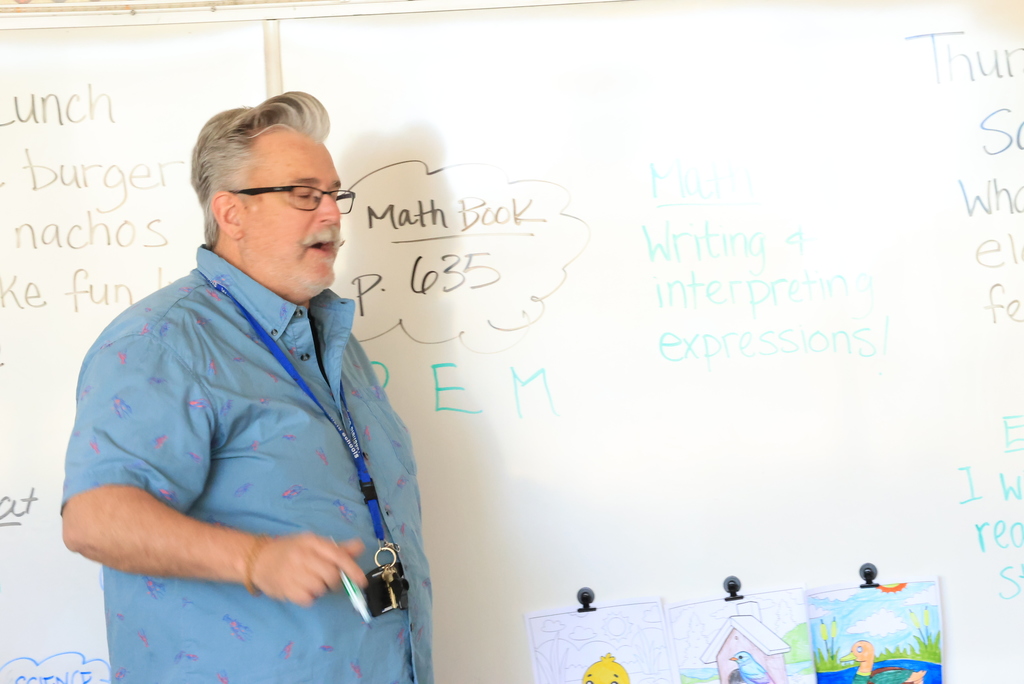 Mr. Yenni discusses writing and interpreting expressions during math class and writes on the white board.