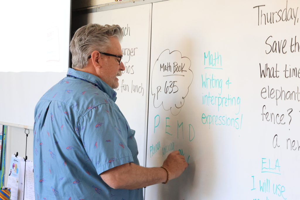 Mr. Yenni discusses writing and interpreting expressions during math class and writes on the white board.