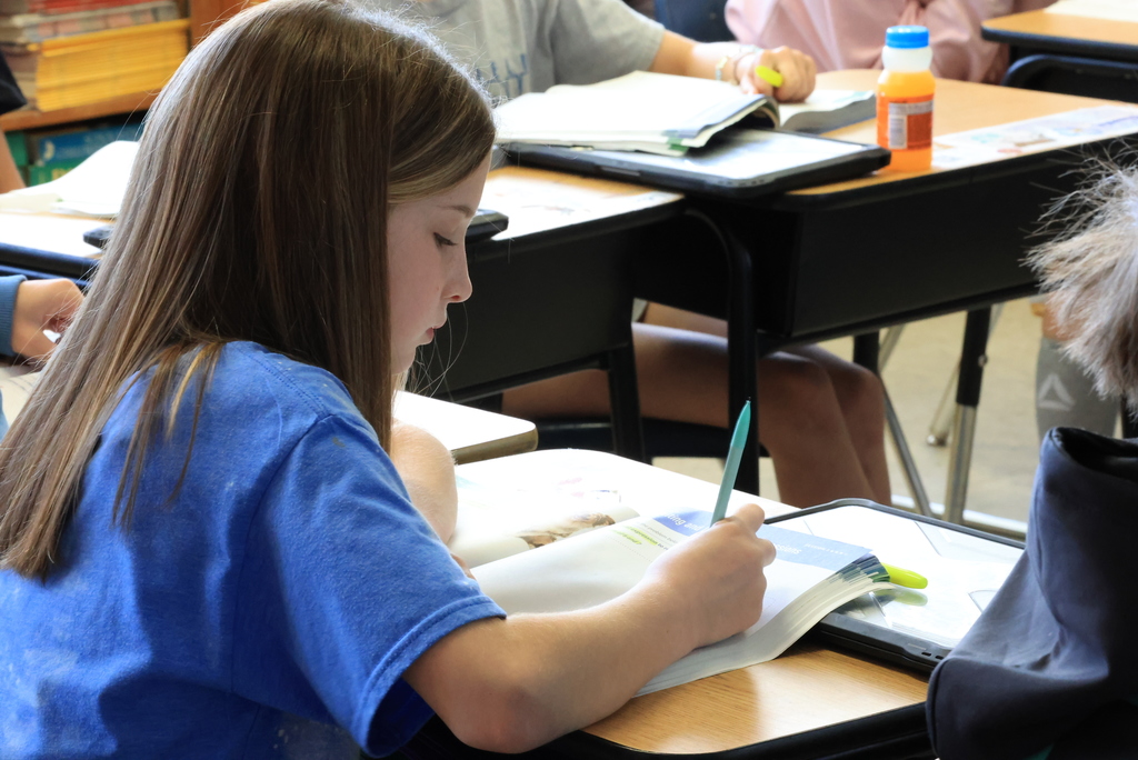 A student writes notes in the math book while listening to Mr. Yenni.