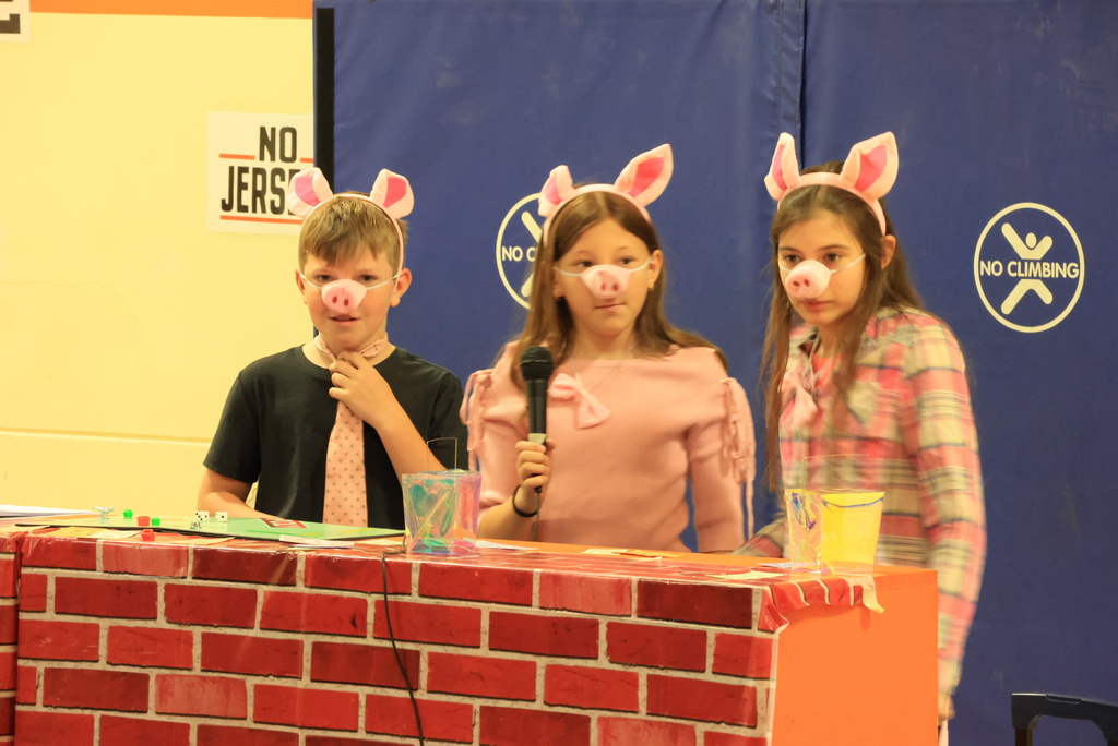 Three students dressed as pigs act out a scene behind a brick prop during the play, 'Blame it on the Wolf."