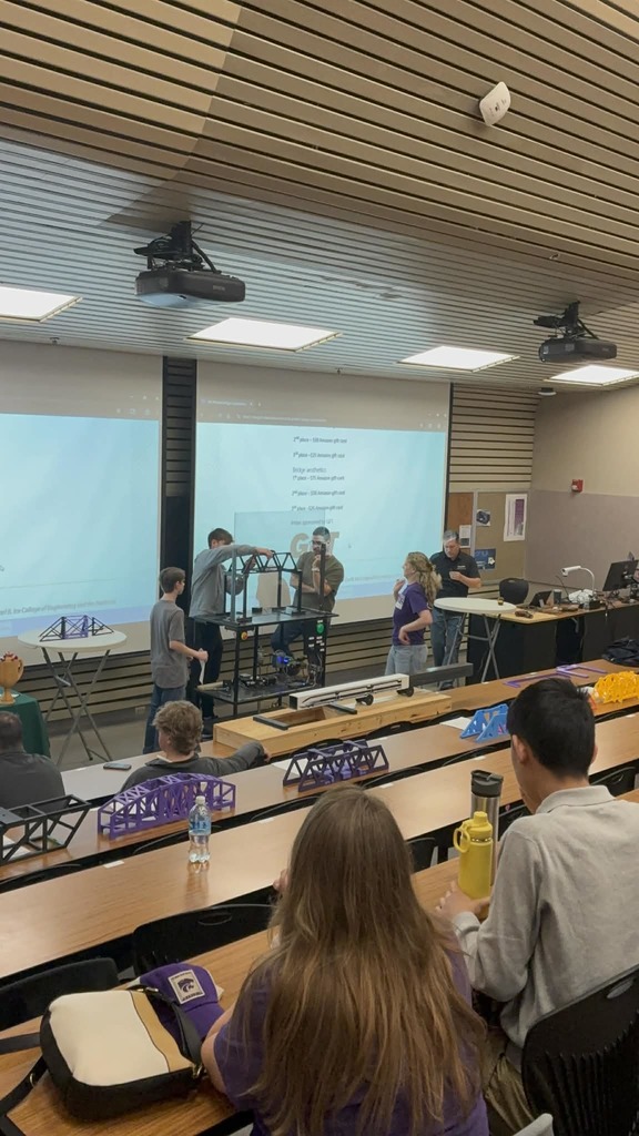 Seniors Caden Peterson and Brody Stenfors test out their bridge at the 3D-Printed Railway Bridge Competition while other contestants watch.