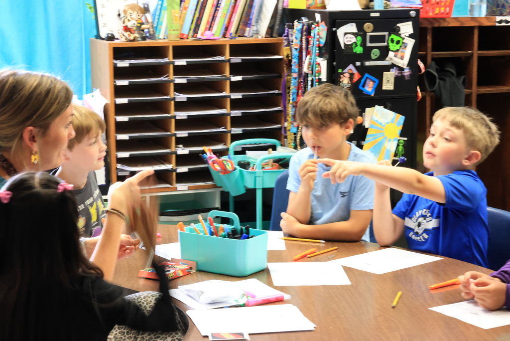 A students points at Mrs. Ehlers as she asks a question during small group reading intervention.
