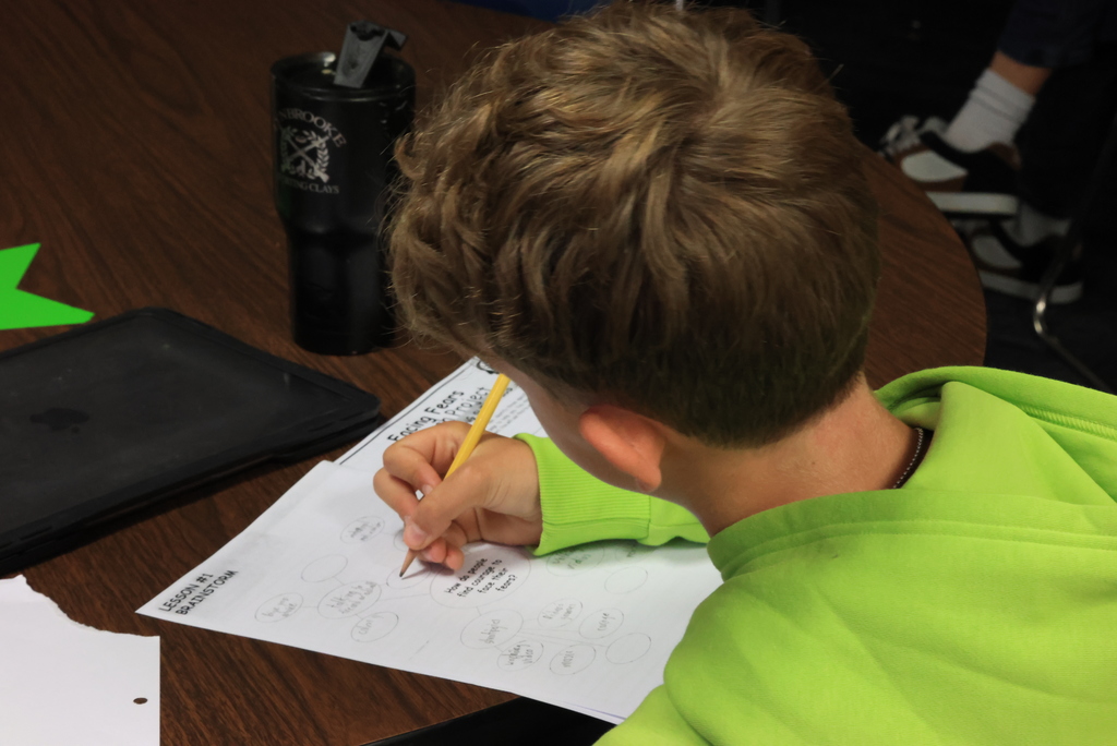 A student writes his ideas on his paper as Mrs. Crabtree talks.