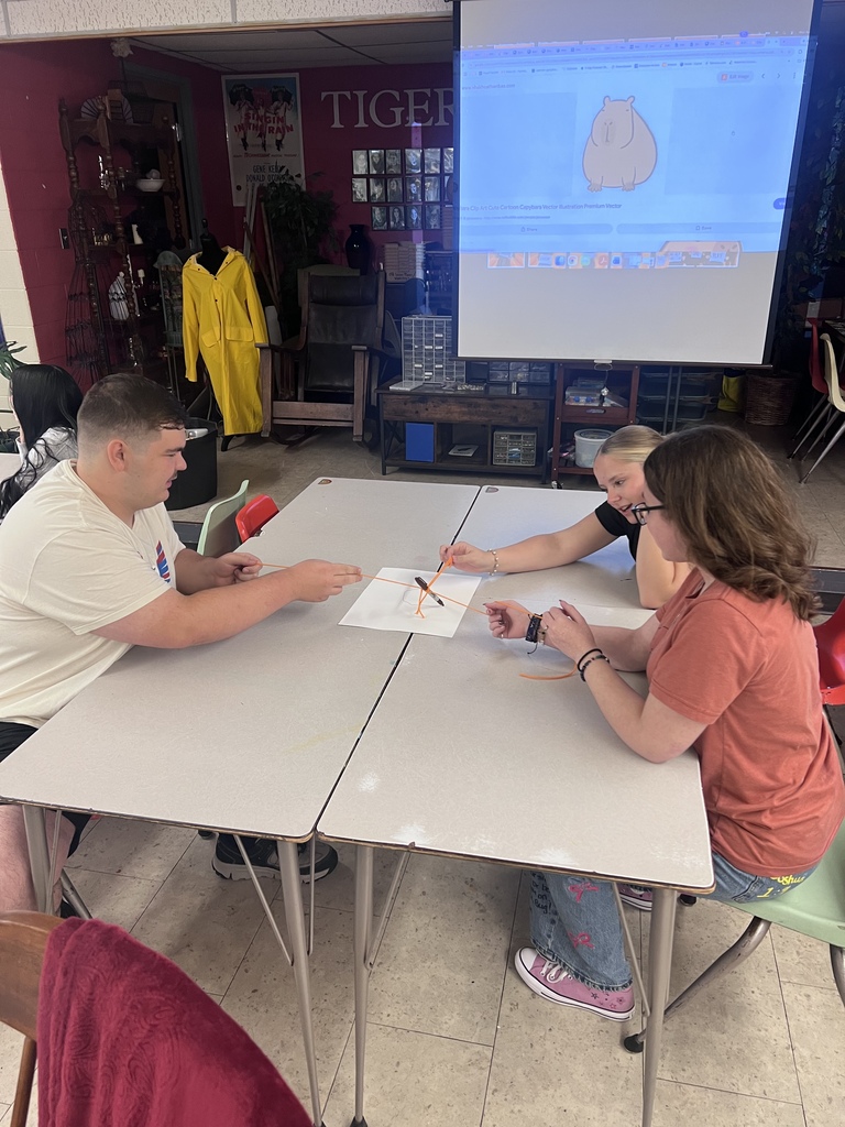 Mrs. Blackburn's debate team attempts to draw an image on the screen using teamwork with string and a marker.
