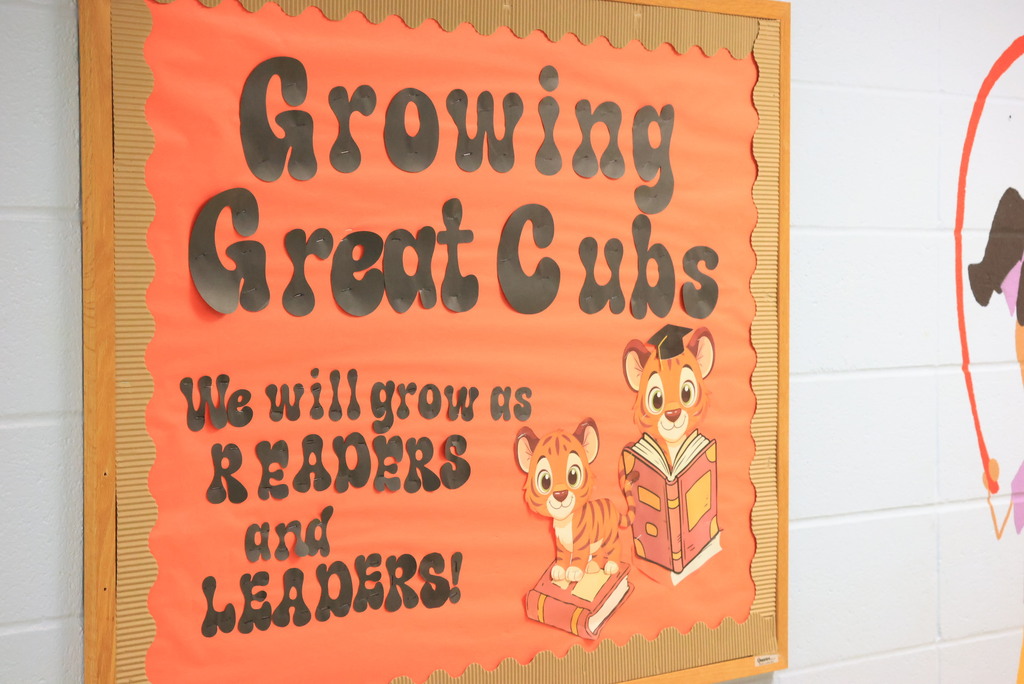 A sign is shown outside of the Pre-K classrooms. It says, GRowing Great Cubs, We will grow as readers and leaders!