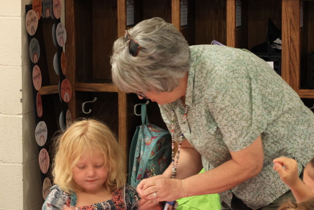 Kindergarten aide Mrs. Wallace shows her students how to put googly eyes on to their number chart.