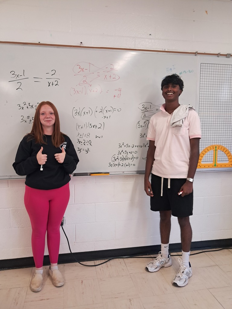 picture of students standing in front of a whiteboard with an math problem on it