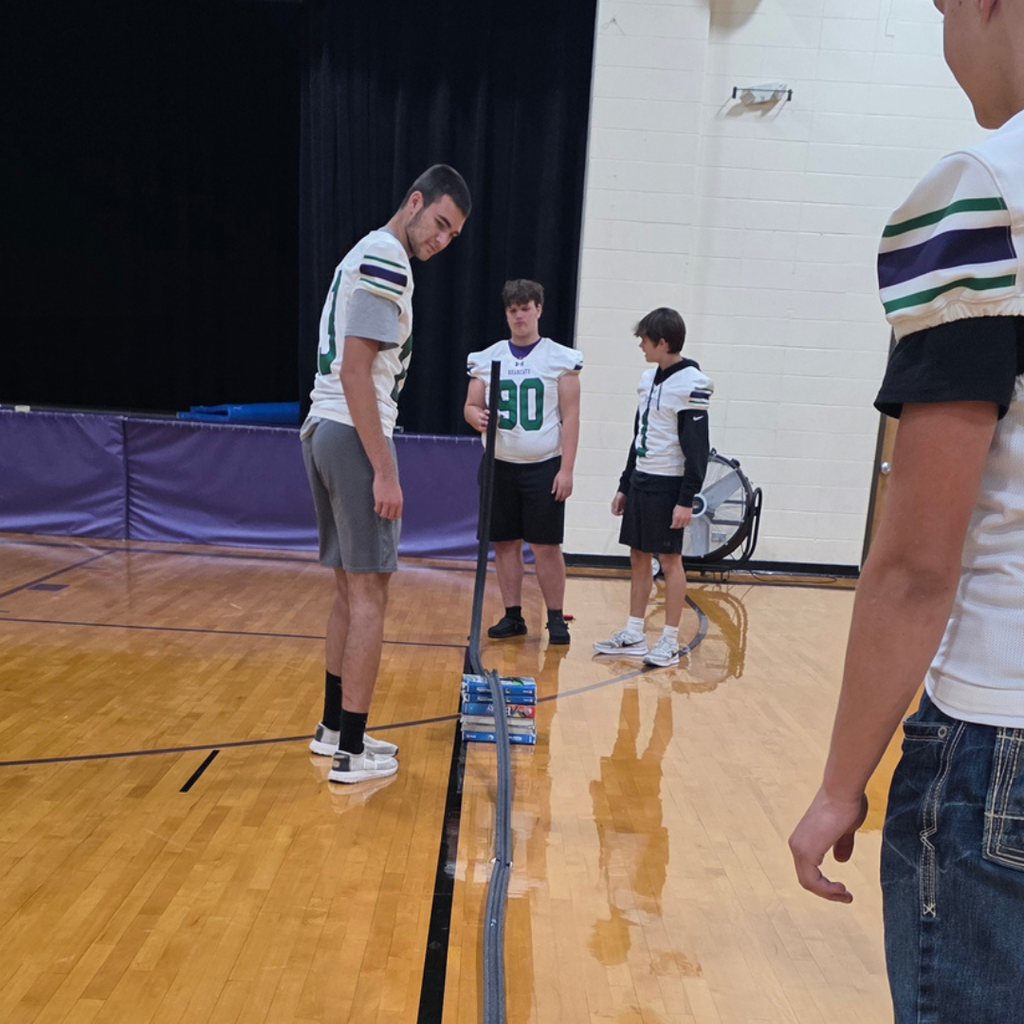 Students standing in a gym testing speed on a ramp.