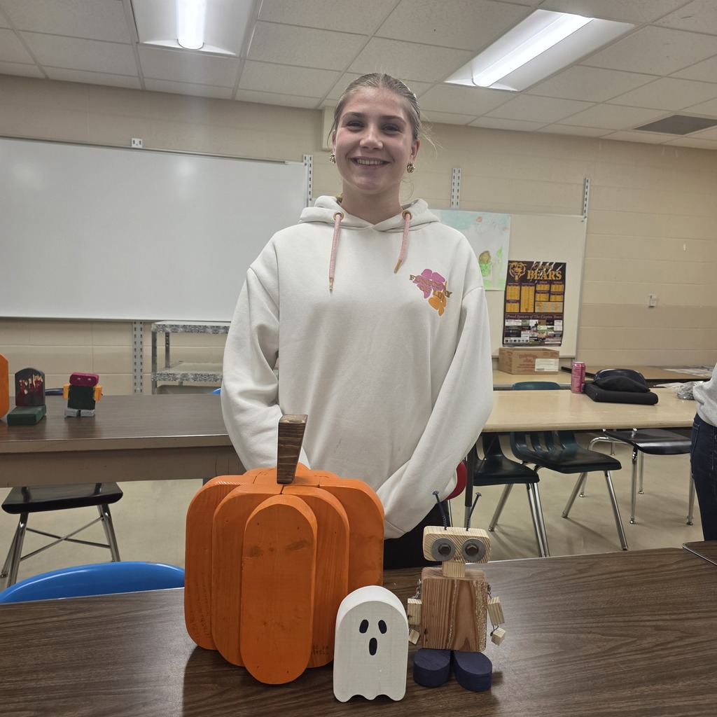 Students holding up pumpkins and wooden crafts made in Woods Class