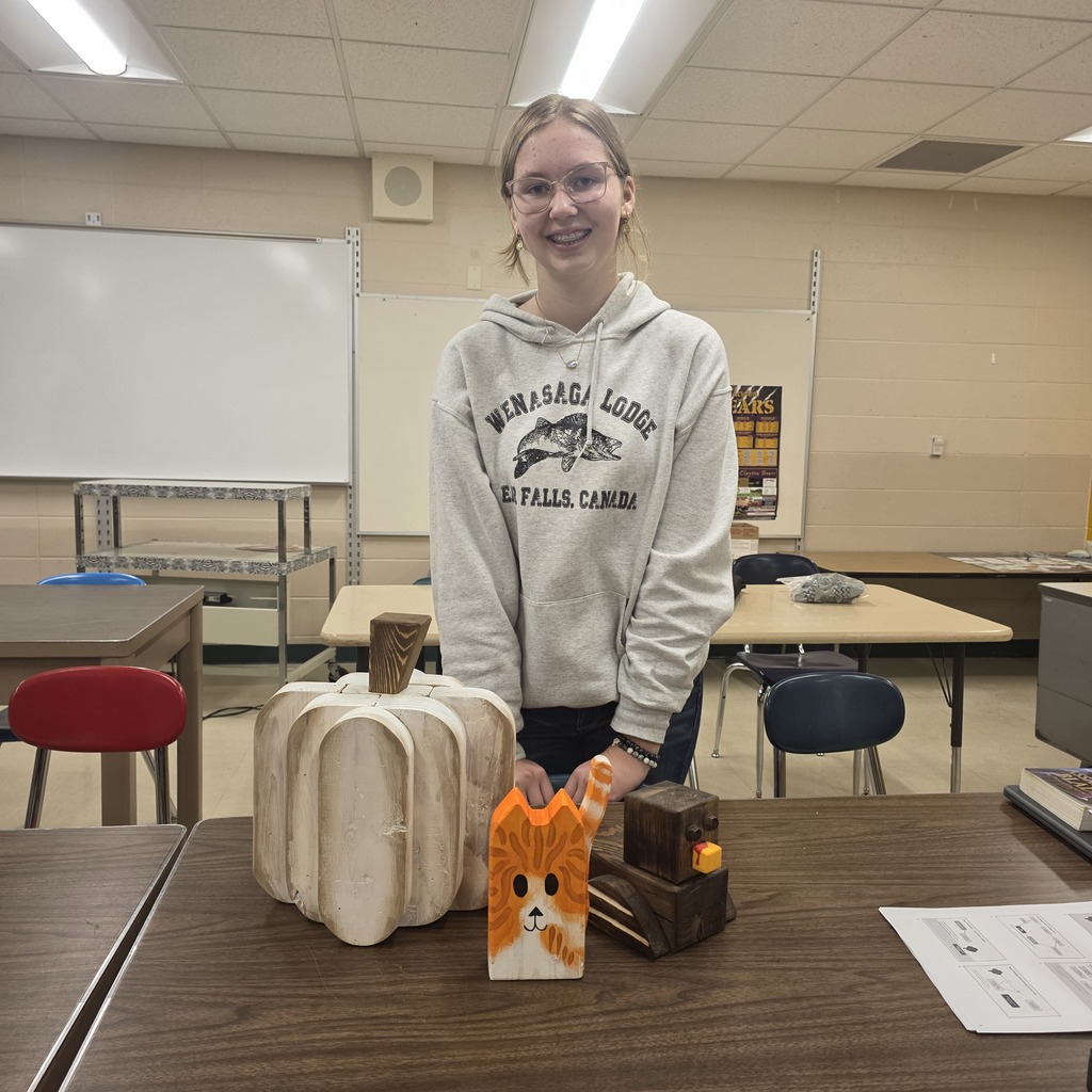 Students holding up pumpkins and wooden crafts made in Woods Class