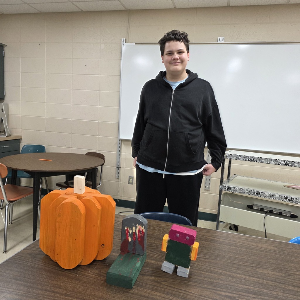 Students holding up pumpkins and wooden crafts made in Woods Class