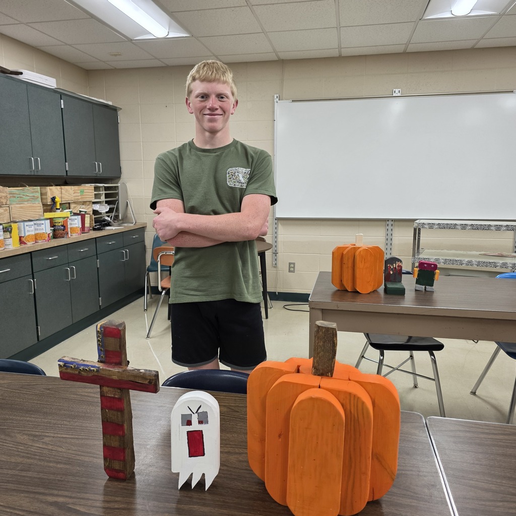 Students holding up pumpkins and wooden crafts made in Woods Class