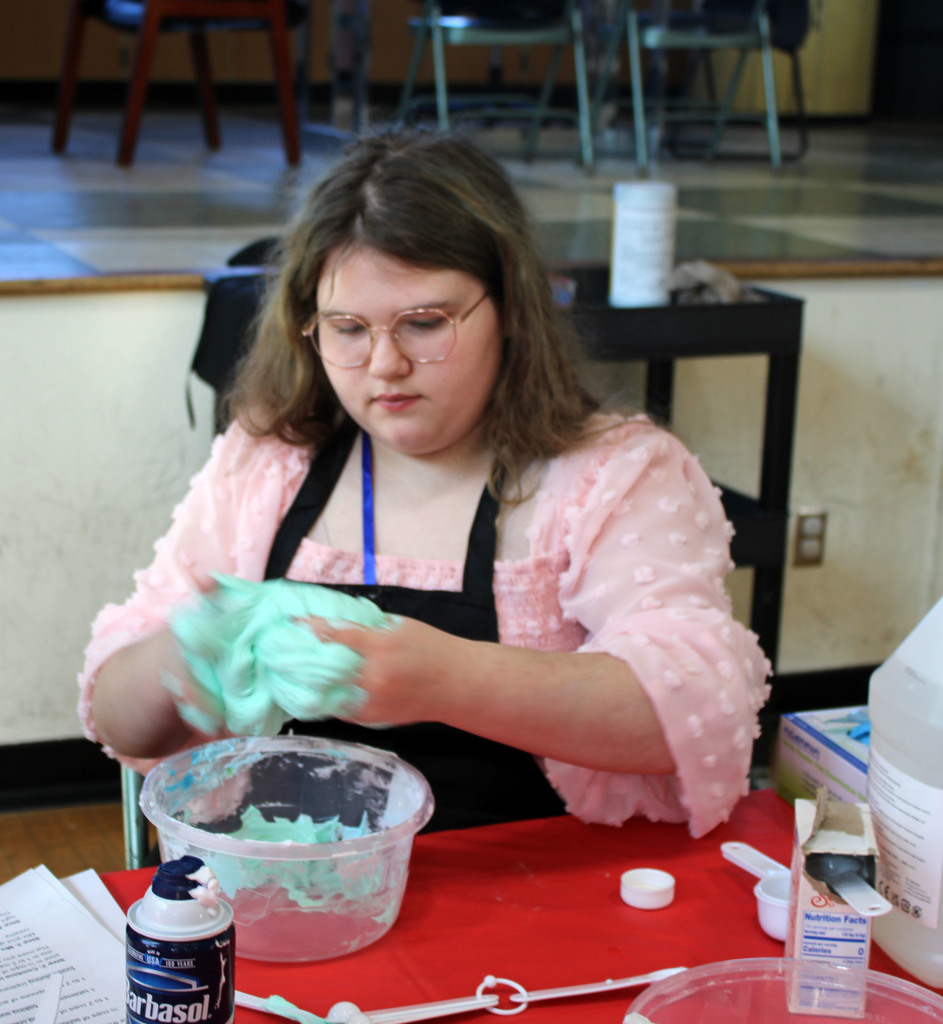 Student mixing together glue, borax, shaving cream, and green dye to make slime.