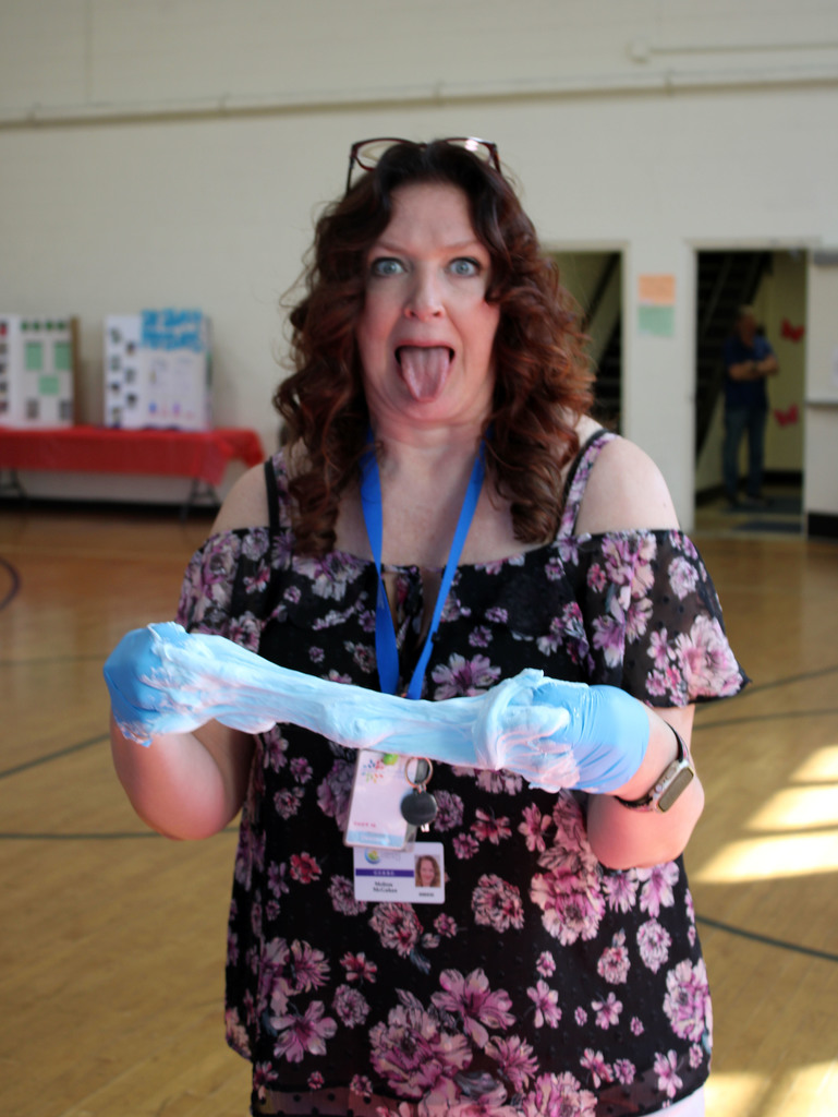 Principal McGahan making blue slime with gloves on while sticking her tongue out at the camera.