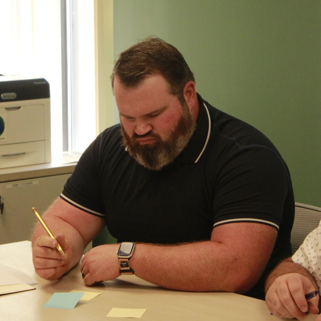 Man writing on small sticky notes stuck to the desk during the Student Success Team meeting.