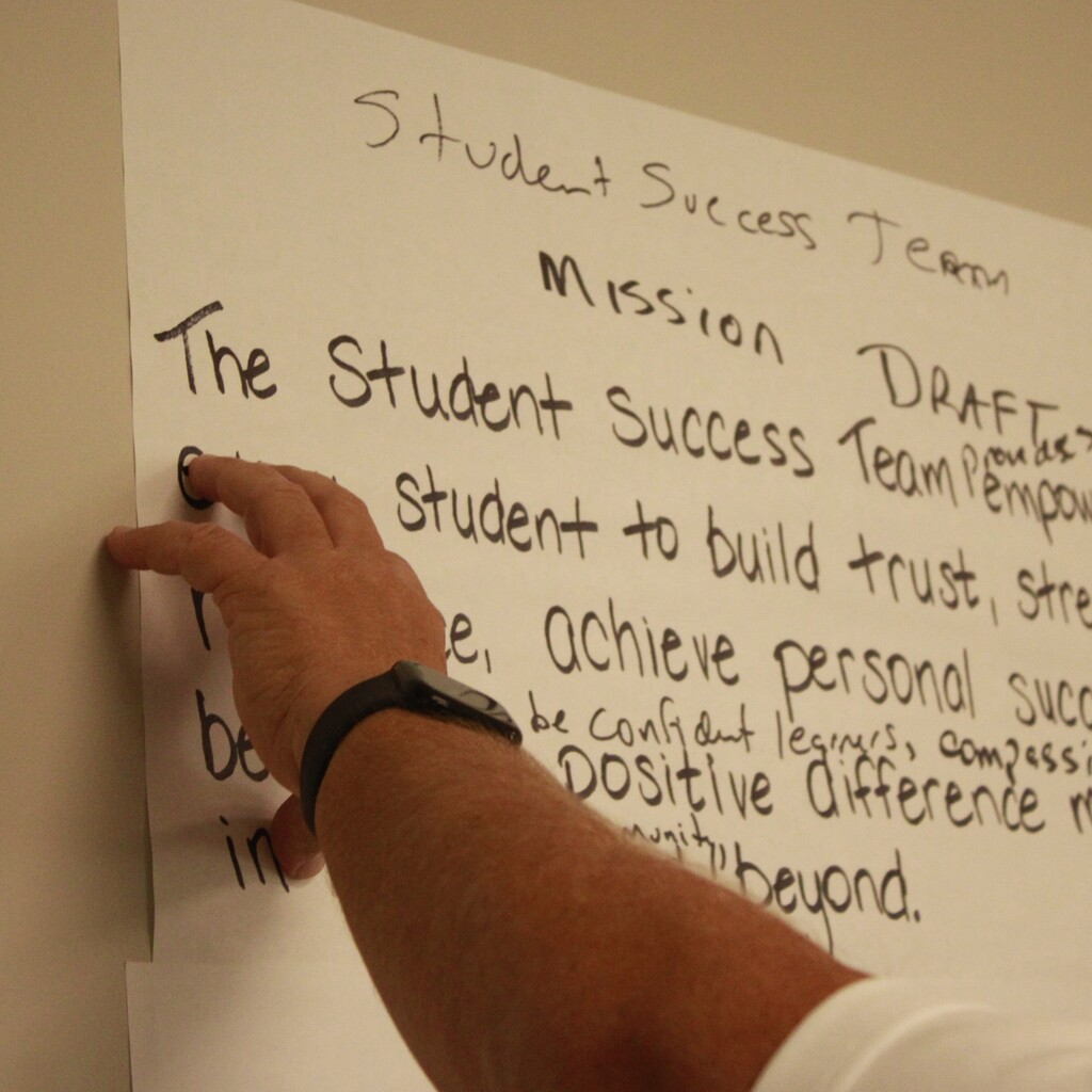 Man point to and talking about content written on massive sticky note during the Student Success Team meeting.