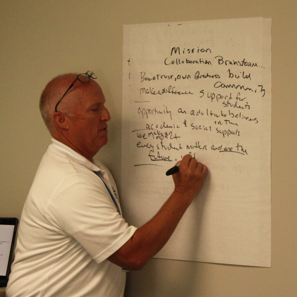 Man writing on massive sticky note during the Student Success Team meeting.