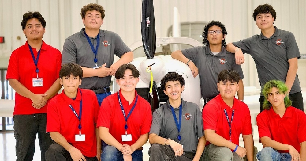 9 young hispanic male students standing in front of an airplane