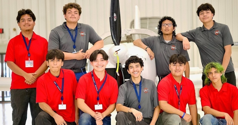 9 young hispanic male students standing in front of an airplane