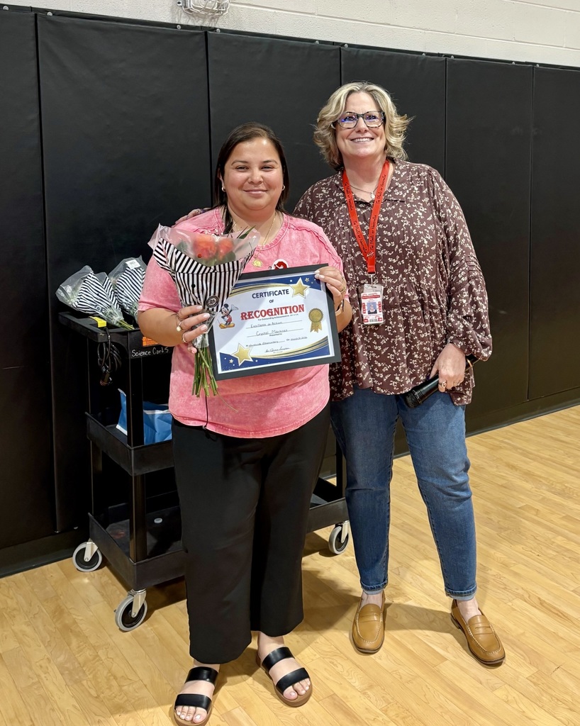 Two women in a room with a black wall. One woman holds a plaque with a bouquet.