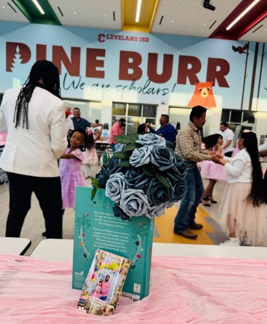Interior of Pine Burr with tables covered in pink. An adult stands behind a table with a flower arrangement and book.