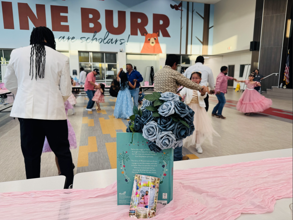 A hall with a sign reading "INE BURR" features a group of people dancing. A pink fabric covers a table with flowers and books.