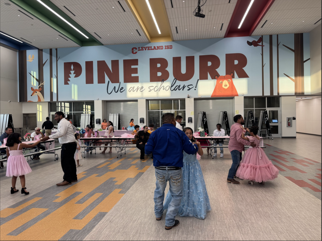 People dance in a large room. A large banner says "PINE BURR" in front of them.
