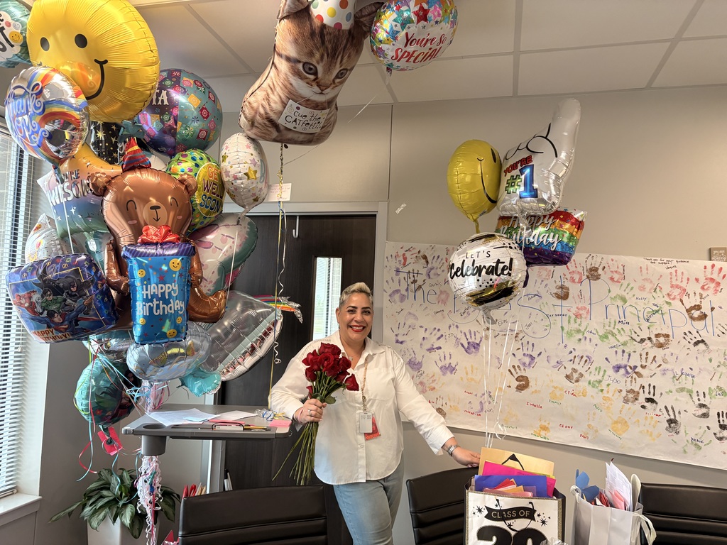Person with roses stands among balloons, with a large board with drawings and messages behind.